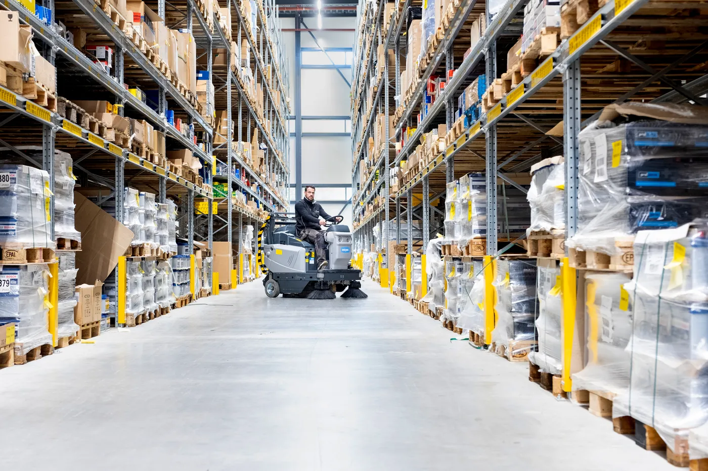 Medewerker veegt een magazijngang tussen hoge palletstellingen met een Meijer VR1300HD