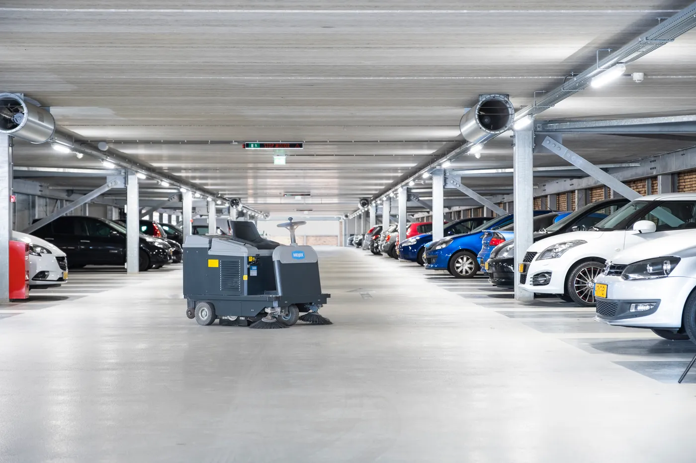 Meijer zitveegmachine in een parkeergarage tussen geparkeerde auto's