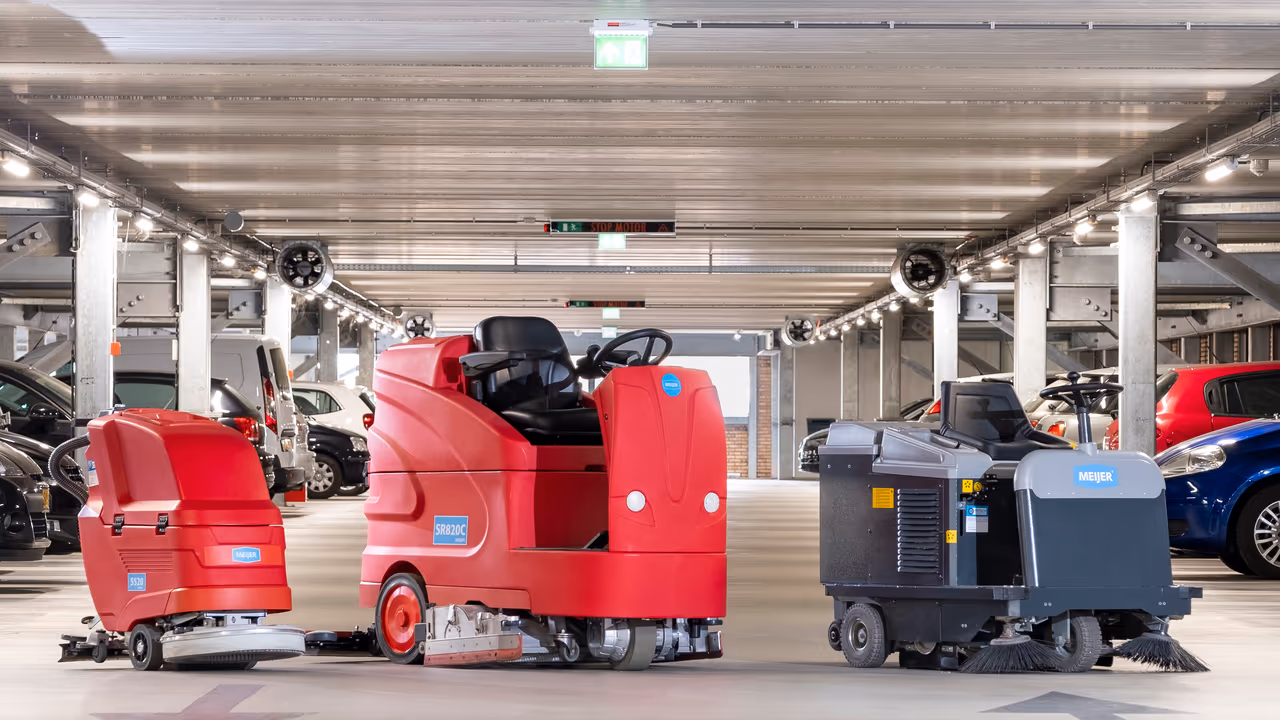 Twee rode Meijer schrobmachines en een Meijer veegmachine opgesteld in een parkeergarage