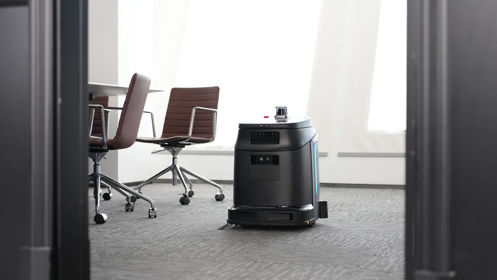 Gausium Phantas op de vloerbedekking van een vergaderzaal, naast de vergaderstoelen